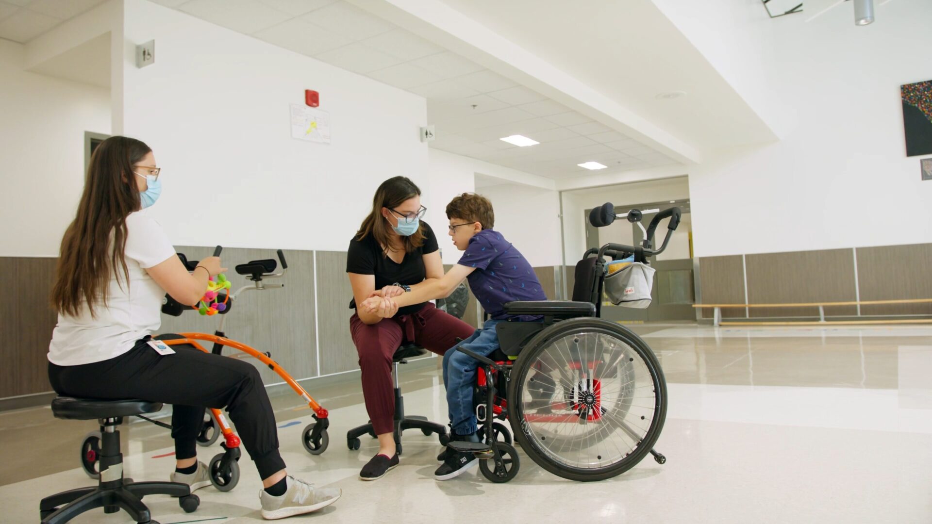 Deux physiothérapeutes effectuent des activités de réadaptation avec un jeune garçon en chaise roulante.